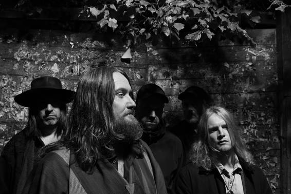 Fünf Männer vor einer bewachsenen Steinmauer